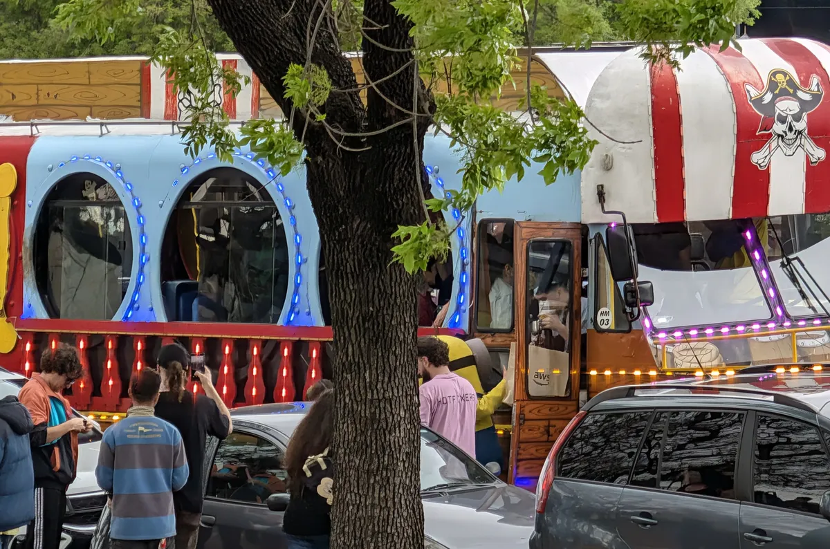 The wardriving bus: porthole windows, LED lights and a pirate flag on its striped roof, parked on a tree-lined street